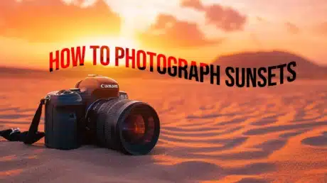 A DSLR camera placed on sandy ground against a vibrant sunset, with the text “How to Photograph Sunsets” floating above