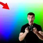 A surprised photographer holding a camera in front of a gradient background that showcases the vividness of 16-bit color depth. The image includes a color scale and a large red arrow pointing to the vibrant colors.