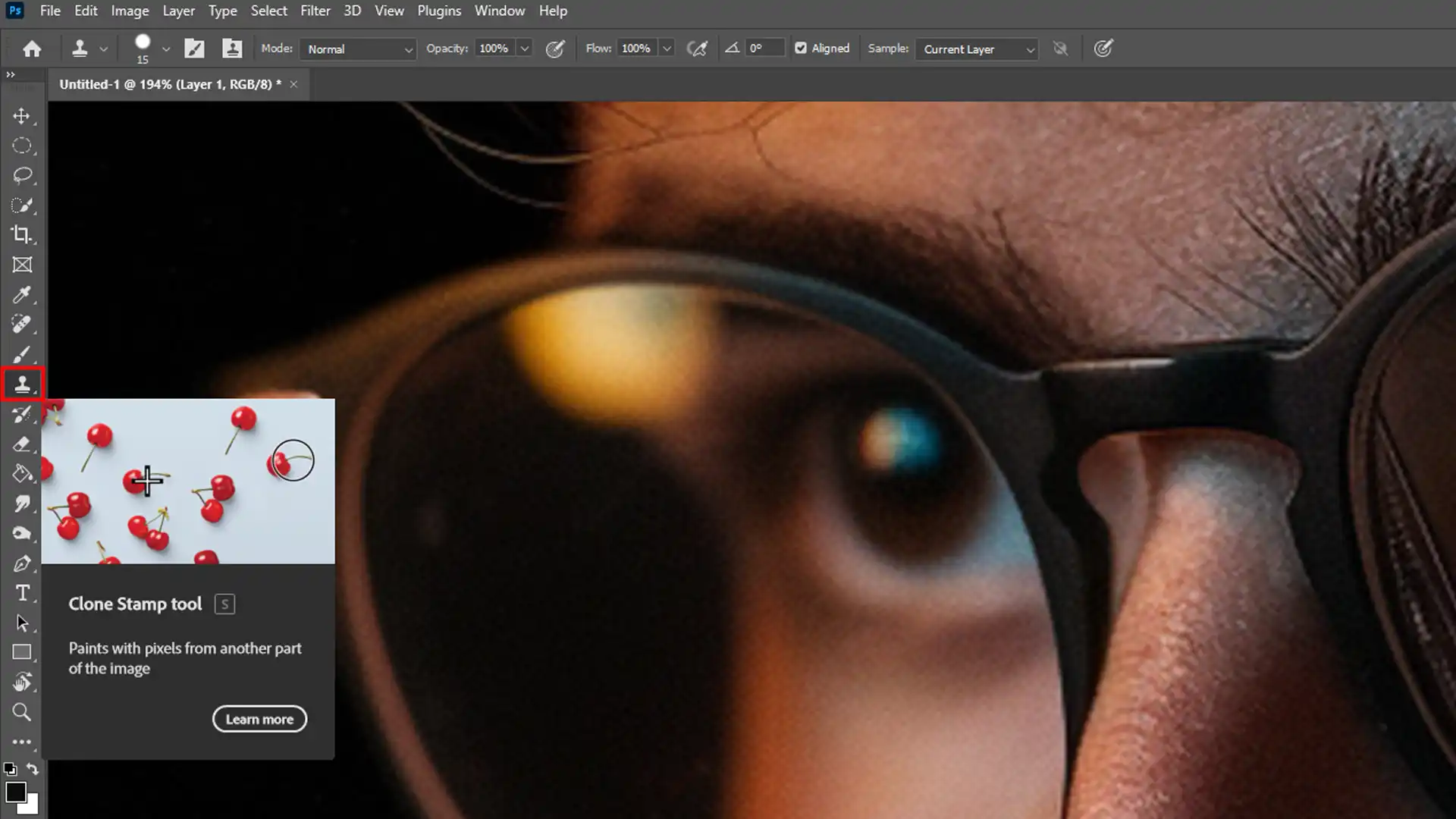 The Clone Stamp Tool is selected in Photoshop, targeting the glasses of a man in a close-up portrait.