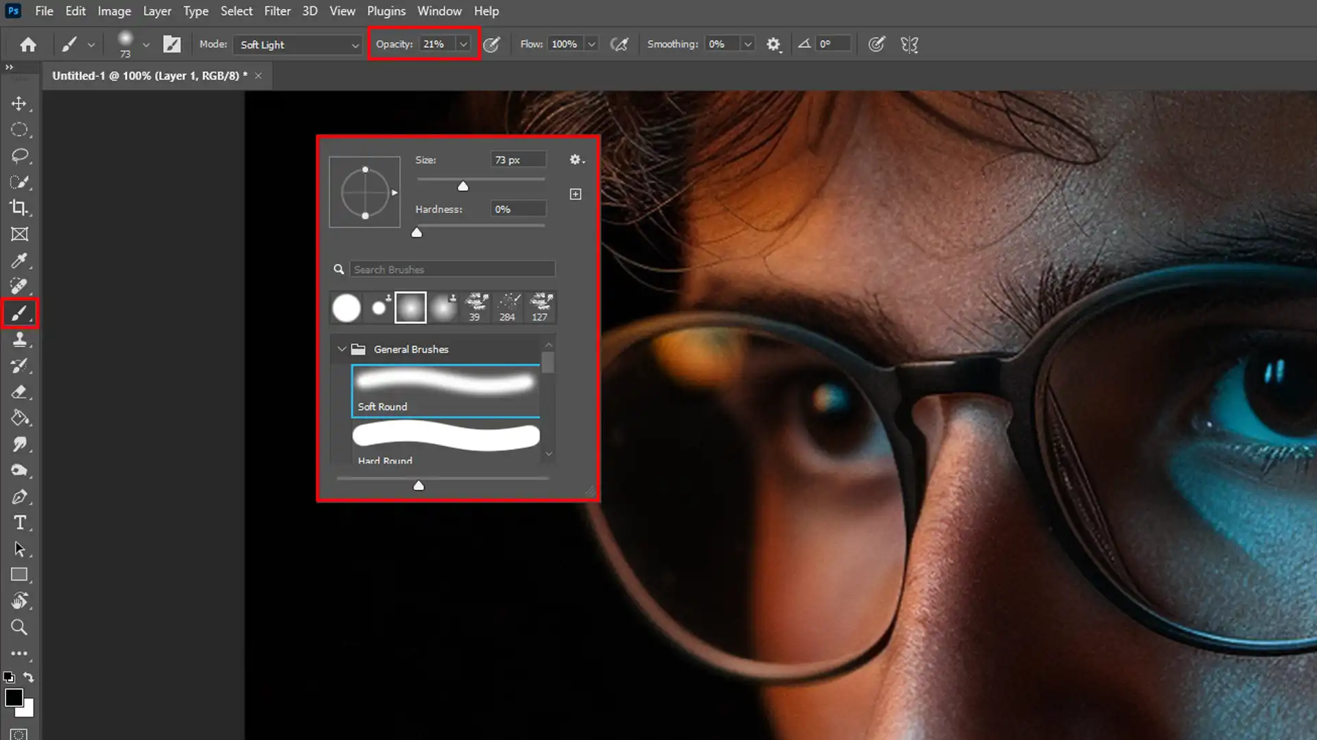 The Brush Tool in Photoshop is selected, with settings adjusted for soft light, focusing on the area around the glasses in a portrait.