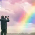 A photographer capturing a vivid rainbow in the sky with a professional camera. The background features soft, colorful clouds with a bright rainbow arching through them, illustrating the use of rainbow photo effects.