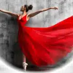 Ballerina in a flowing red dress performing in front of a textured wall with a white vignette effect added in Photoshop.