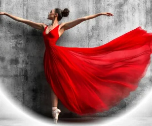 Ballerina in a flowing red dress performing in front of a textured wall with a white vignette effect added in Photoshop.